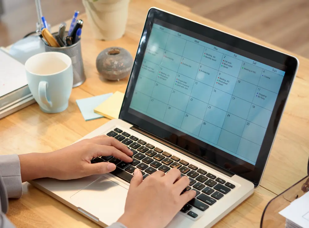 Someone booking an appointment on a laptop calendar at a sunlit desk.